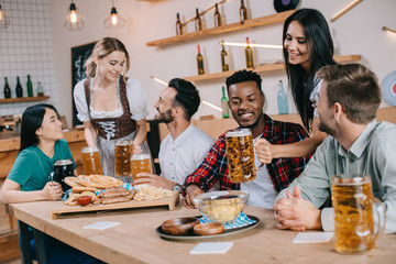 two attractive waitresses serving beer for multicultural friends in pub