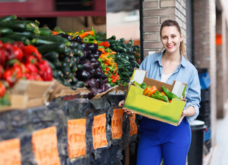Female is looking on shelves with produts and standing with box in the market.