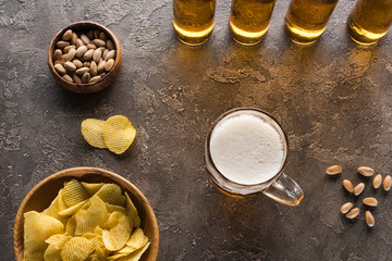 top view of bowls with nuts and crisps near mug and bottles of beer on brown surface