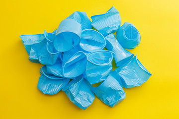 Detail of broken blue plastic disposable cups over a yellow background.