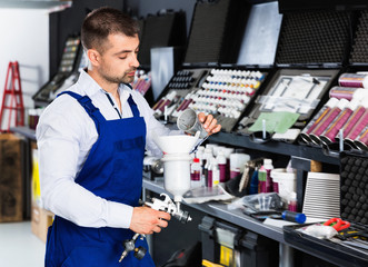 Confident auto mechanic of car painting workshop pouring paints in paint-spray gun
