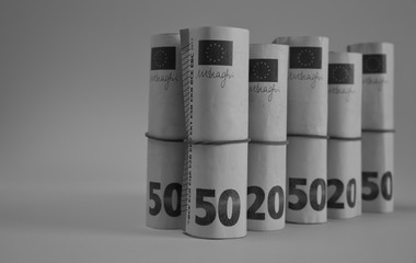Banknotes of 50, 20 and 10 euros rolled in rolls and tied with elastic rubbers stands isolated, monochrome balck and white