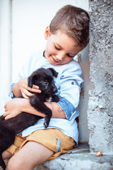 Obraz premium Cute boy holding his pet, little black puppy on the street. Kids and pets