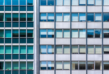 A grid office windows in two modern glass and steel buildings side by side with contrasting colors