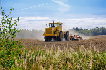 A farm tractor cultivates land after harvesting grain.