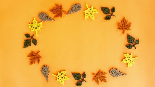 Stop motion animation of beautiful colorful autumn leaves standing in a circle and spinning around its axis on orange background