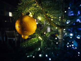 Golden globe hanged on Christmas fir tree in the city with lights defocused in background