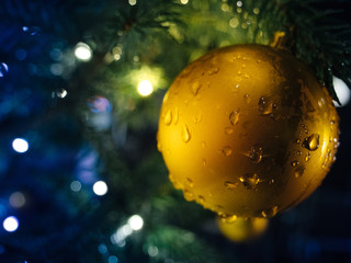 Golden globe hanged on Christmas fir tree in the city with lights defocused in background
