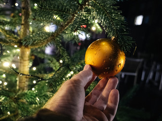 Man hand holding sparkling golden globe hanged on a tree with defocused blur bokeh in background