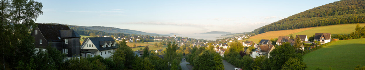 Fototapeta na wymiar Wide panorama of a valley in Sauerland, Germany, with the spa village of Graftschaft and the pilgrimage Wilzenberg mountain at sunrise