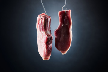 uncooked pork steaks on metal hooks on dark black background