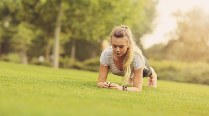 Fit woman doing plank exercise in the park on the green grass in the morning - Healthy lifestyle