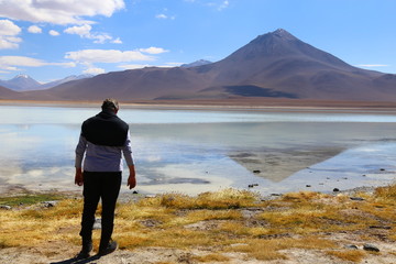 Fototapeta na wymiar Man standing in front of the Laguna Blanca lake in Bolivia. White waters and reflections. In the background mountain and blue sky. 