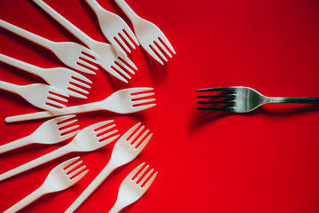 A lot of plastic forks and one metal on a red background.