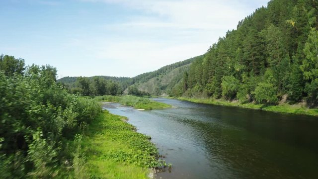 A drone flies over a riverbed at the foot of a mountain range. Riverbank in dense vegetation. Beautiful landscape in the morning.