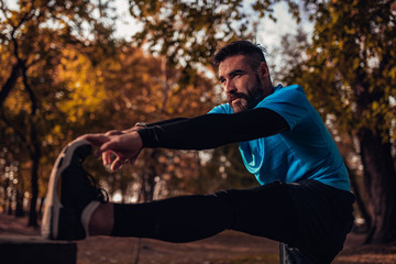 Sporty man stretching legs in park.