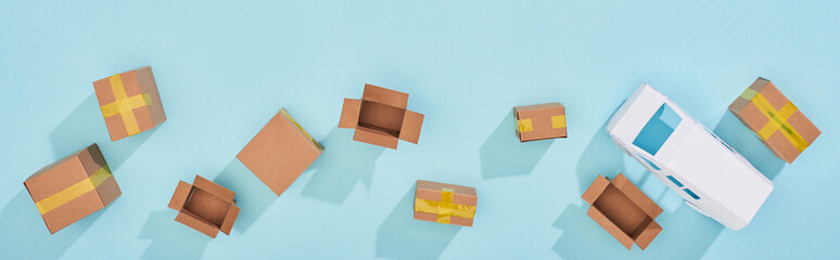 Panoramic shot of closed and open cardboard parcels near mini van on blue background © LIGHTFIELD STUDIOS