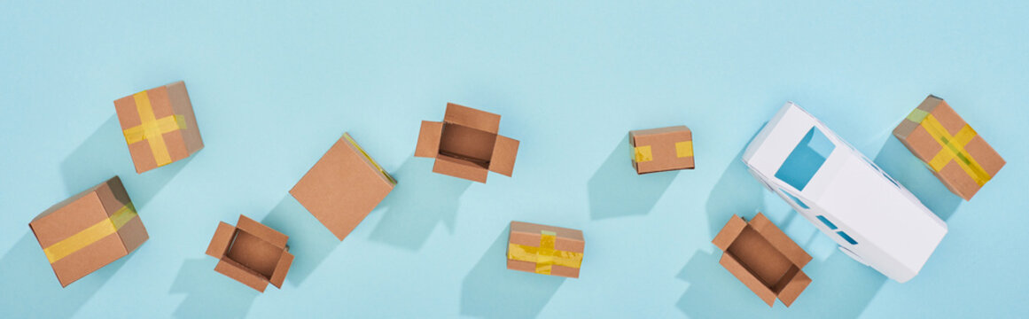 Panoramic shot of closed and open cardboard parcels near mini van on blue background