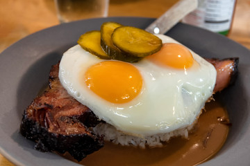 Gourmet smoked barbecue brisket loco moco, consisting of rice, bbq beef, eggs, and pickles in a shallow pool of gravy