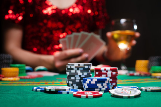 A girl in an evening red dress plays with cards in a casino raising the stacks with croupier chips. Gaming business casinos, night clubs