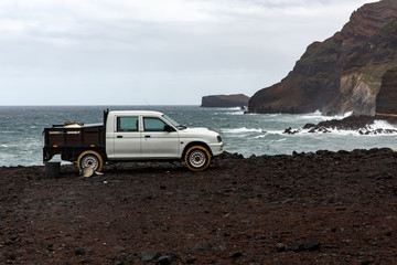 White pickup near the ocean, rocky shore.