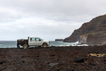 White pickup near the ocean, rocky shore.