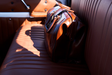 Business travel concept with brown leather bag on old car seat