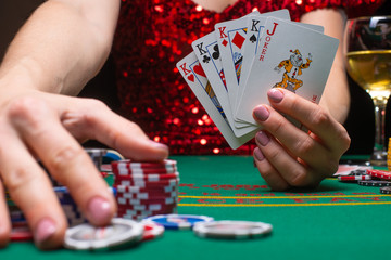Casino games. A girl in a red evening dress and plays poker in a night casino. opens cards and takes winnings