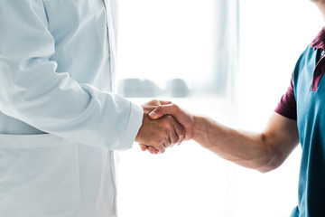 cropped view of doctor in white coat shaking hands with man
