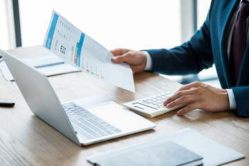 cropped view of businessman holding paper with credit report lettering and counting on calculator