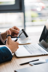cropped view of man holding scissors near credit card and gadgets on desk