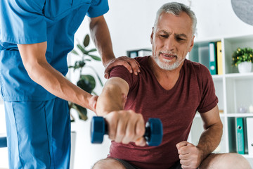 selective focus of mature man working out with dumbbell near doctor