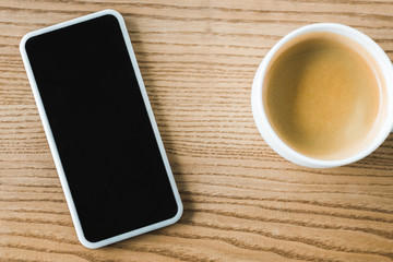 Fototapeta na wymiar top view of smartphone with blank screen near cup of coffee