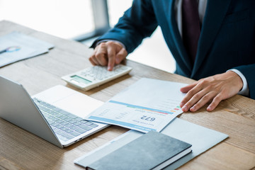 Selective focus of man holding paper with credit report lettering and counting on calculator