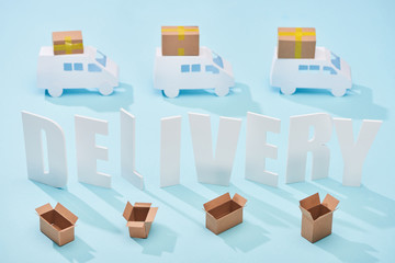 white delivery inscription between mini trucks and open cardboard boxes on blue background