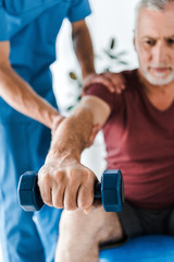 selective focus of mature man training with dumbbell near doctor