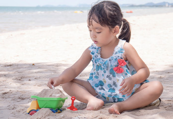  little girl playing with a toy excavator in the sand at the beach of Cha-am, Thailand.