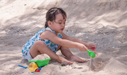  little girl playing with a toy excavator in the sand at the beach of Cha-am, Thailand.