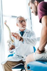 low angle view of man sitting near doctor gesturing while holding spine model