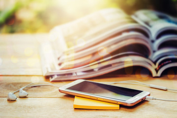 close up of smart phone and yellow note pad  over blurred stack of magazine and cup of coffee on...