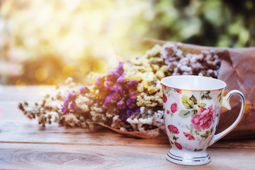 close up of  a cup of tea and flowers on wooden table against sun light