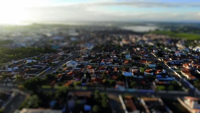 Tilt shift aerial view of a low-income urban area in Cruz das Almas, Bahia, Brazil. Show houses, small buildings in the neighborhood, and green environnement. Drone slowly moving down.