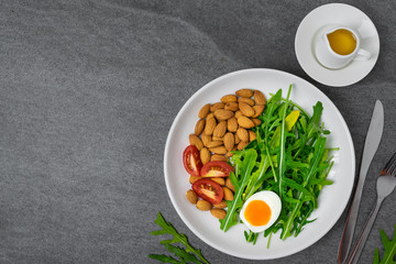Arugula salad with almonds and tomato,boiled egg in white dish on tile table.