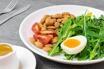 Arugula salad with almonds and tomato,boiled egg in white dish on tile table.