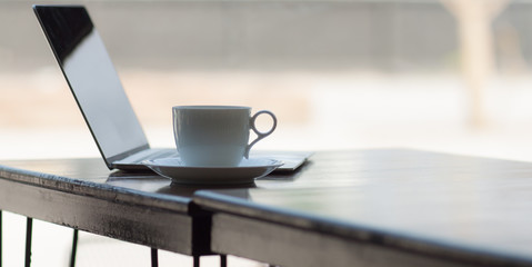 A cup of coffee and a laptop with morning sunlight.