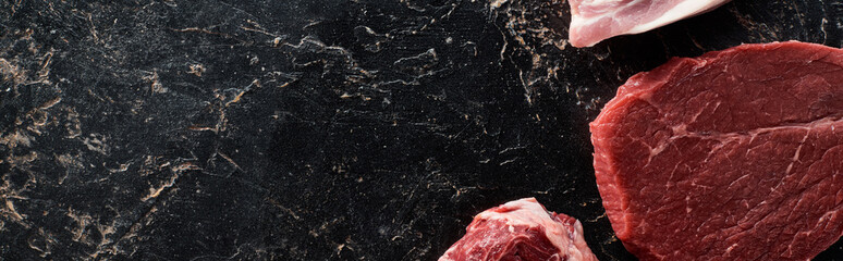 panoramic shot of uncooked meat parts on black marble surface