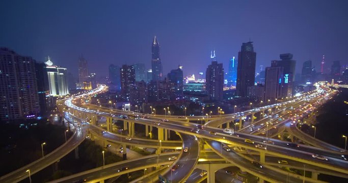 Shanghai city traffic moving in busy intersection junction surrounded by tall modern buildings at night in slow motion, China