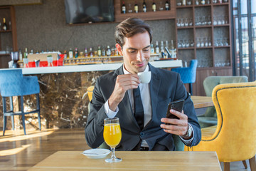 Handsome young businessman using his cell phone in hotel cafe