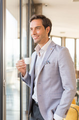 Handsome young businessman drinks coffee in front of the hotel window