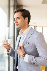 Handsome young businessman drinks coffee in front of the hotel window